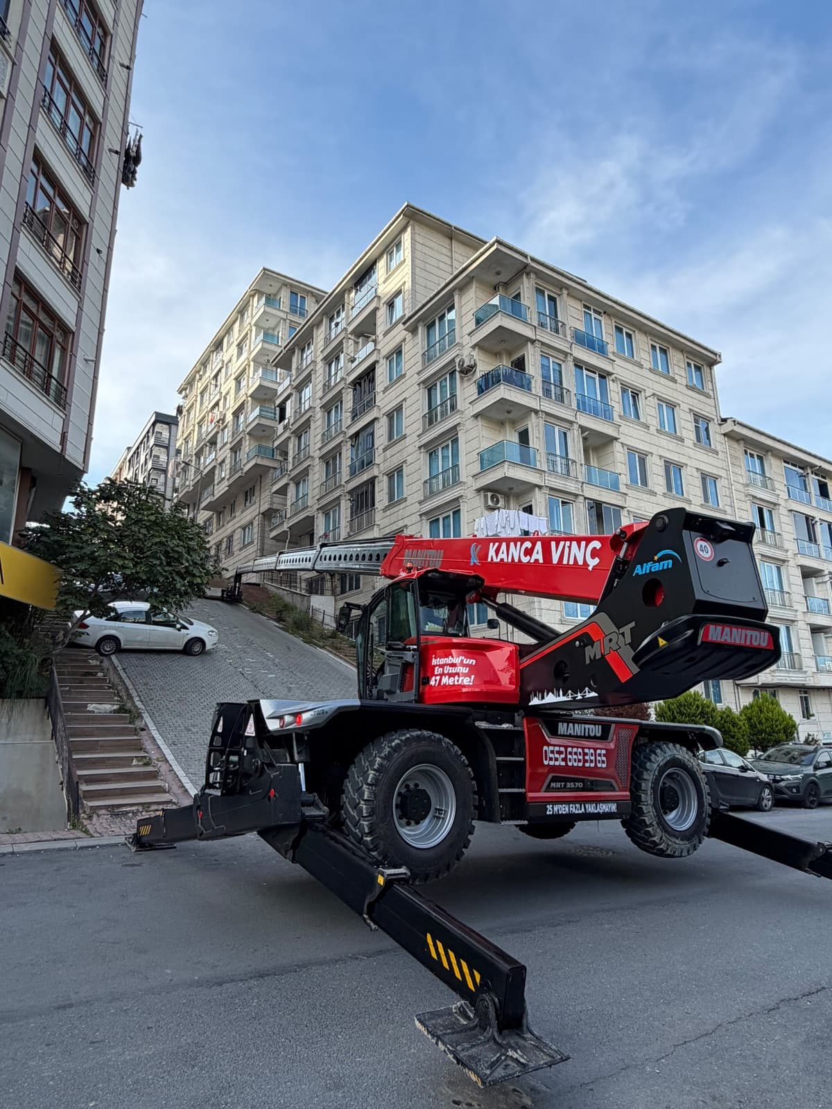 Kanca Vinç döner platformlu Manitou MRT apartman önünde ayakları açılmış, bom uzatılmış halde çalışmaya hazır